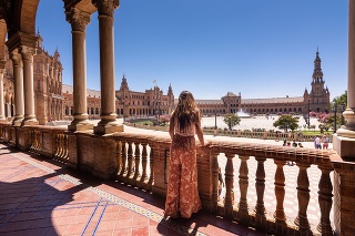 A tourist enjoys the spectacular views of the plaza from the elevated walkway. The Plaza de España is a plaza in María Luisa Park, in Seville, Spain. Built in 1928, the Plaza de Espana is huge and takes on a half-elliptic shape, which represents the embrace of Spain and its ancient colonies. The square is surrounded by a long canal that is crossed by four bridges.
