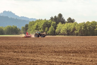 Tractor sowing in empty field on countryside, small trees in background.