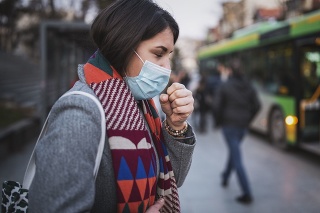 Side view of woman wear face mask and coughing while standing in the town, looking down