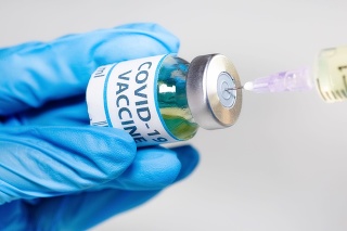 Doctor hand wearing medical gloves in close up view hold a vaccine bottle vial while transferring medication to an injection syringe used for treatment of Covid-19 patients