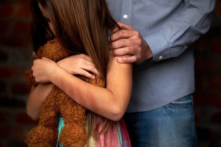 Abused little girl with her abuser gripping her shoulder