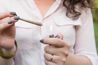 The young person smoking medical marijuana joint outdoors. The young woman smoke cannabis blunt, close-up. Cannabis is a concept of herbal alternative medicine.