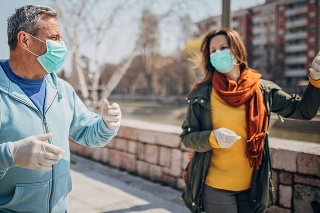 Man and woman, two people with protective mask walking and talking on the street in safe distance.