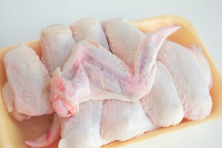 Chilled chicken wings in a yellow tray, fresh meat from the store on a white table. High protein in chicken.