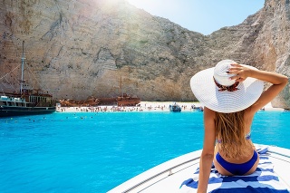 Beautiful, blonde woman in a bikini on a boat enjoys the view to the famous shipwreck beach, Navagio, in the island of Zakynthos, Greece