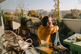 Photo of a woman drinking first morning coffee, eating 'take out' food and reading daily news online - on the balcony of her apartment while enjoying springtime sun