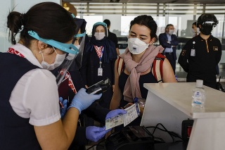 Zamestnankyňa leteckej spoločnosti kontroluje cestujúcich v rukaviciach a s prekrytím tváre. 