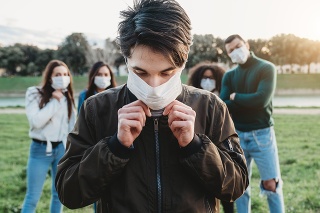 Young adult man wearing a pollution mask to protect himself from viruses. His friends are in the background. They all are wearing masks. Conceptual image of protection against pandemic virus.