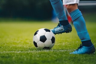 Close up of legs and feet of football player in blue socks and shoes running and dribbling with the ball. Soccer player running after the ball. Sports venue in the background