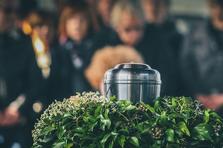 A metal urn with ashes of a dead person on a funeral, with people mourning in the background on a memorial service. Sad grieving moment at the end of a life. Last farewell to a person in an urn.