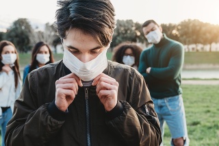 Young adult man wearing a pollution mask to protect himself from viruses. His friends are in the background. They all are wearing masks. Conceptual image of protection against pandemic virus.