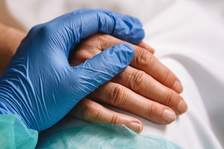 Close up of a doctor hand with blue glove giving support and love to a patient at hospital. Coronavirus pandemic concept.