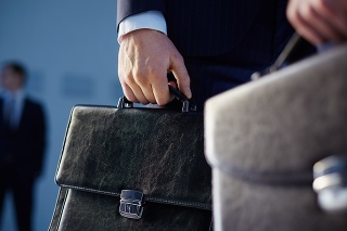 Cropped image of business partners carrying briefcases on the foreground while their colleague standing on the background 