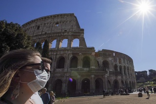 Turisti s ochrannými rúškami kráčajú popri antickom Koloseu v Ríme.