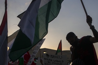 Palestínski stúpenci na proteste držia transparenty a palestínske zástavy.