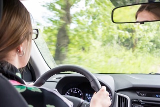 Girl with glasses at the wheel of the car. View from behind the seated driver
