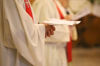 young priest with a cassock and hands joined in prayer during Holy Mass