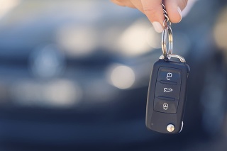 Female car salesperson handing  over the new car keys. There is a new car behind her out of focus. Close up with Copy space