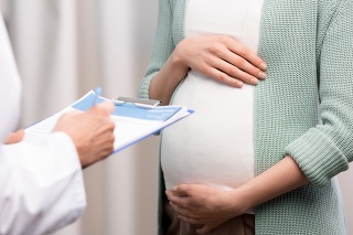 cropped shot of doctor writing down while pregnant woman holding stomach