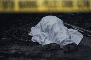 The dead body is seen lying on the ground behind a cordon tape.