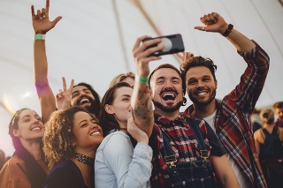 Group of young adult friends are taking a group selfie on a smartphone while they are at a festival.