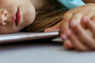 Cute youg girl sleeping in bed with smartphone. Front view of 7 years old child is lying on the sofa and holding smartphone with eyes closed.