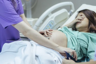 Doctor examining belly of expectant mother in hospital room. Thailand.