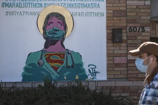 Muž s ochranným rúškom na tvári kráča okolo grafitu, ktorý nabáda ľudí zostať doma  v maďarskom meste Érd.