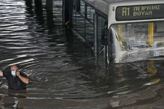 Vodič sa brodí vo vode a telefonuje po evakuácii pasažierov z autobusu, ktorý uviazol v zaplavenom podchode v Aténach.