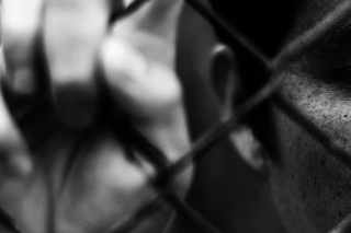 Depressed man standing behind a fence, hand grabs steel mesh cage,close up on face in white tone, abuse concept