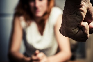 Young woman is sitting hunched at a table at home, the focus is on a man's fist in the foregound of the image
