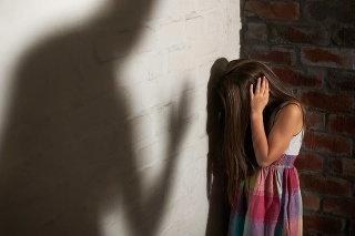 Abused little girl huddled over while the shadow of her abuser looms towards her
