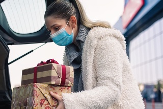 Teenage girl packing Christmas gifts in a car after shopping. She wears a protective mask to protect from corona virus COVID-19.