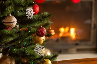 Closeup image of golden and red baubles on Christmas tree in front of burning fireplace. Beautiful Christmas background