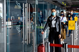 People traveling by airplane during COVID 19, wearing N95 face masks, carrying luggage and waiting in line at airport terminal, keeping distance.