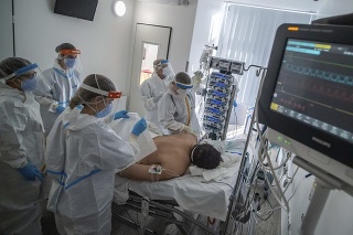 Doktori a zdravotné sestry v ochrannom oblečení sa starajú o covid pacienta napojeného na ventilátor na jednotke intenzívnej starostlivosti.