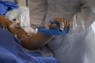Lekár v špeciálnom ochrannom odeve drží ruku pacienta s ochorením COVID-19 na jednotke intenzívnej strostlivosti (ilustračné foto)