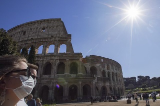 Turisti s ochrannými rúškami kráčajú popri antickom Koloseu v Ríme.