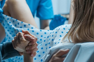 Emergency In the Hospital: Woman Giving Birth, Husband Holds Her Hand in Support, Obstetricians Assisting. Modern Delivery Ward with Professional Midwives.