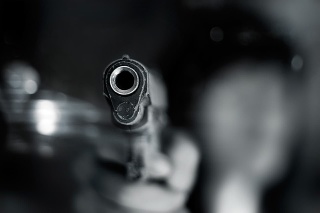 Black and white, woman pointing a old gun to front with one Hand on dark background