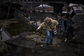 Žena prechádza cez zničený most počas siedmeho dňa ruskej invázie na Ukrajine.