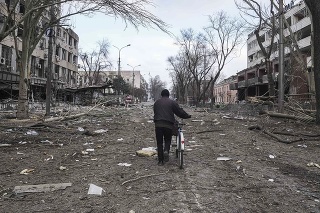 Muž kráča s bicyklom po ulici poškodenej ostreľovaním v Mariupole na Ukrajine.

