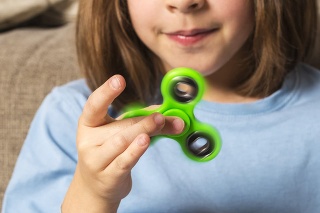 Little girl playing with green fidget spinner toy to relieve stress at home