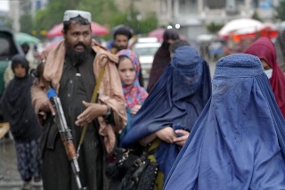 Ženy sa v utorok 3. mája 2022 prechádzajú starým trhom, zatiaľ čo bojovník Talibanu stojí na stráži v meste Kábul v Afganistane.