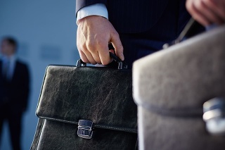 Cropped image of business partners carrying briefcases on the foreground while their colleague standing on the background 