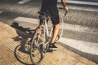 Man riding an old road bike and crossing a crosswalk in the city with black clothes, at sunset.