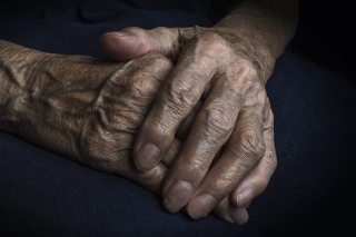 Hands of an old woman with wrinkled and wrinkles on dark background.