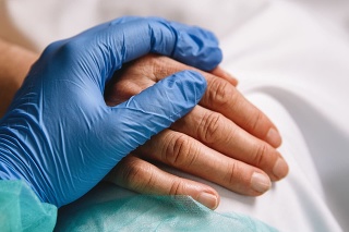Close up of a doctor hand with blue glove giving support and love to a patient at hospital. Coronavirus pandemic concept.