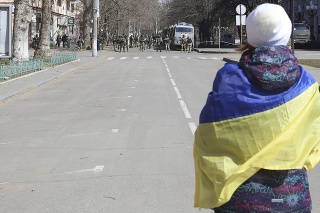 Na archívnej snímke z 19. marca žena s ukrajinskou vlajkou stojí  pred ruskými vojakmi počas zhromaždenia proti ruskej okupácii v ukrajinskom meste Cherson.
