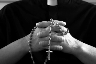Silhouette of a praying priest with rosary beads in hands